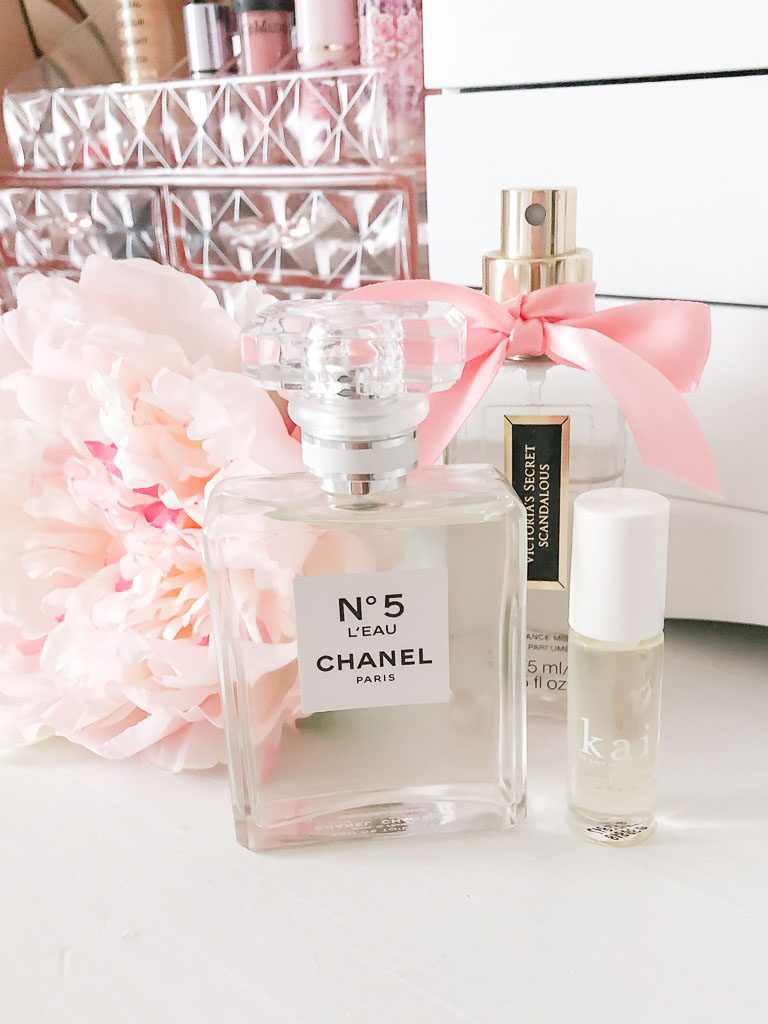 Perfume sitting on a white dresser with a pink peony.